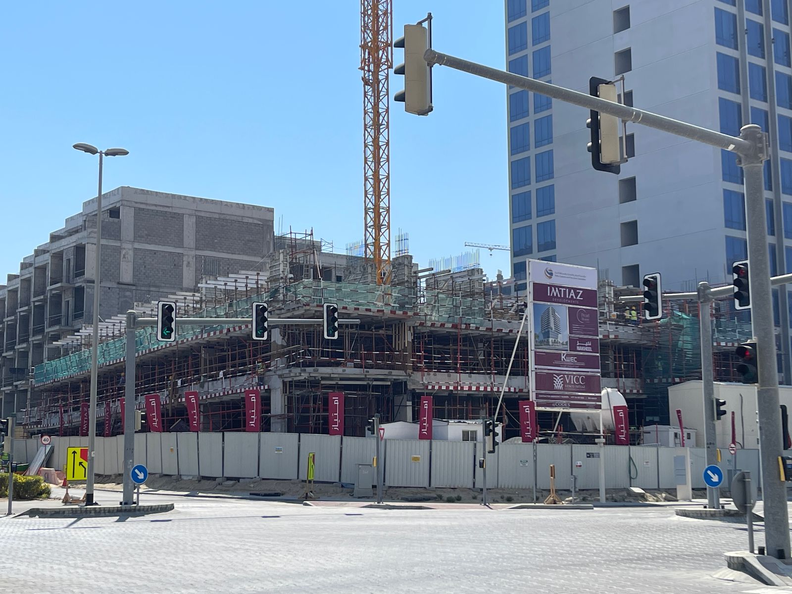 Pearl House By Imtiaz Construction site of a building with scaffolding, cranes, and traffic lights in an urban area under blue sky.